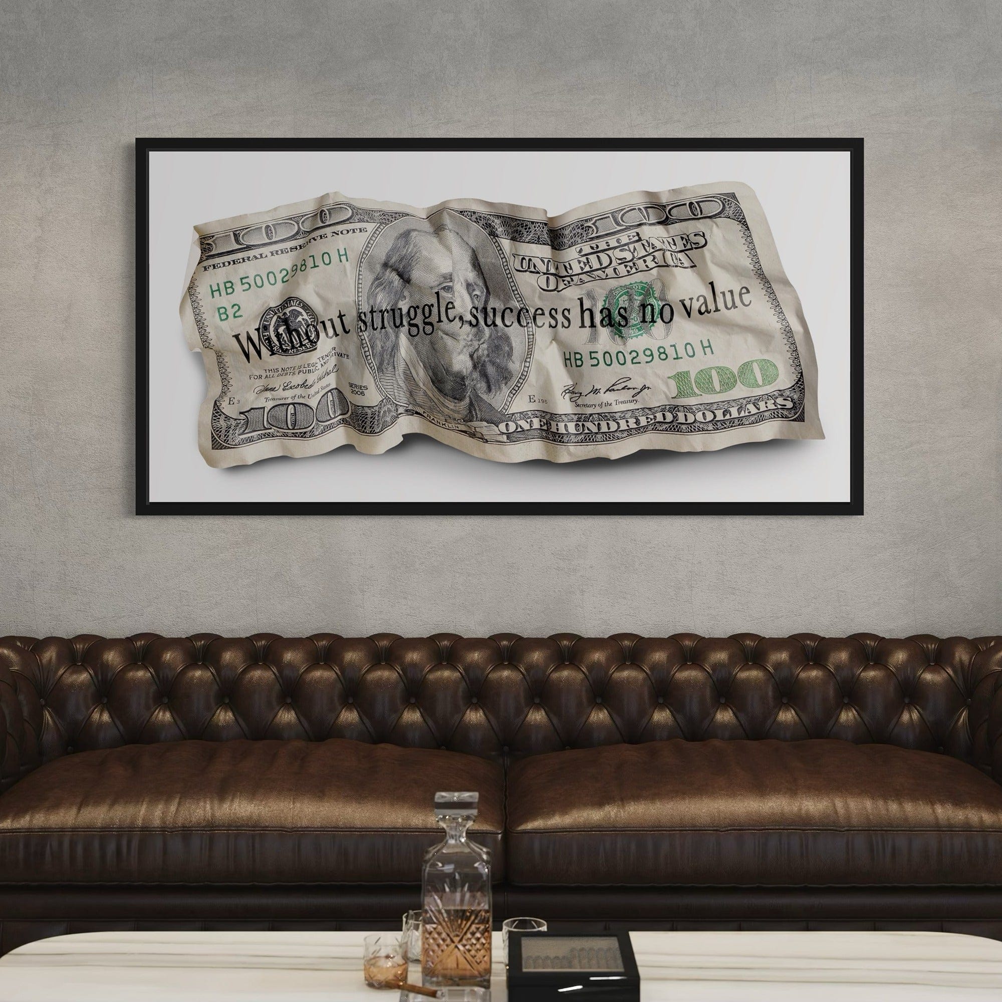 Framed dollar bill artwork with motivational quote above a brown leather sofa.
